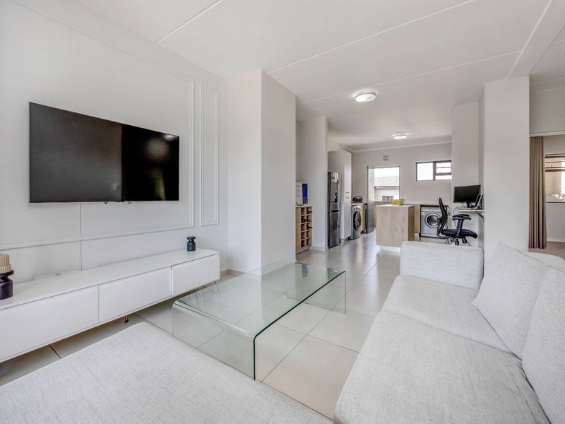 Modern open-plan living area featuring tiled floors, decorative wall molding, and a seamless transition into a functional kitchen and laundry space.