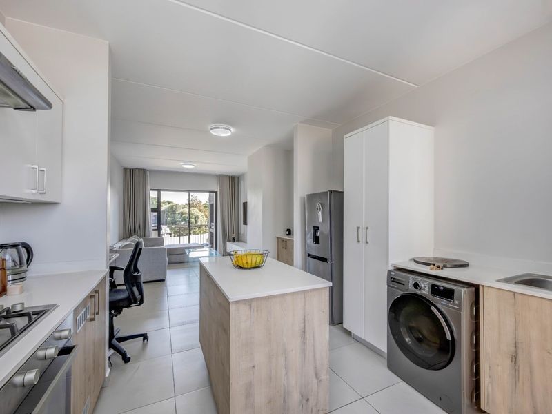 Modern open-plan kitchen and living area featuring contemporary cabinetry, a central island, tiled flooring, and direct access to a balcony through sliding glass doors.