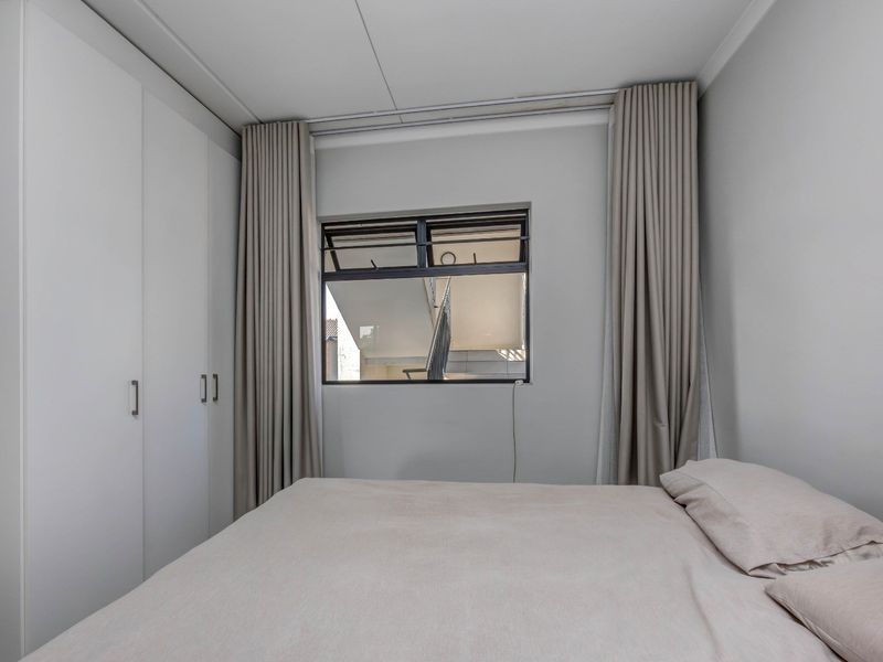 A well-maintained bedroom featuring neutral walls, built-in cupboards for storage, and a top-hung window with floor-to-ceiling curtains.