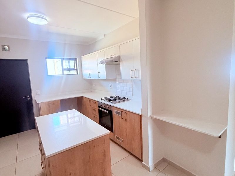 Modern kitchen featuring light wood cabinetry, white stone countertops, a central island, built-in gas hob, oven, and sleek tiled flooring.