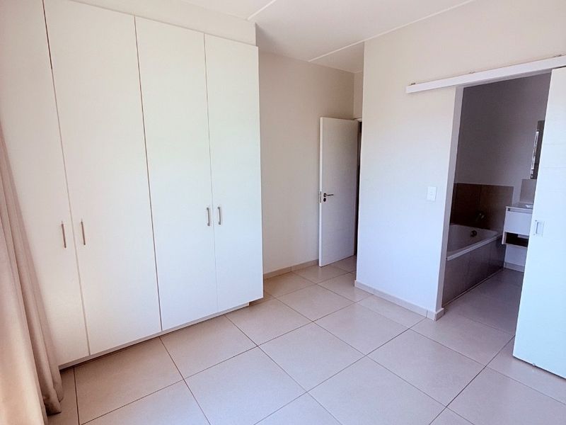A bright, empty bedroom featuring neutral tiled flooring, ample built-in cupboard space, and direct access to an en-suite bathroom.