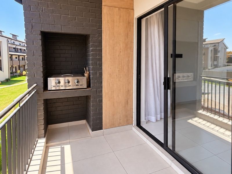 A modern, well-maintained balcony featuring a built-in braai, tiled flooring, and large sliding glass doors providing seamless indoor-outdoor flow.