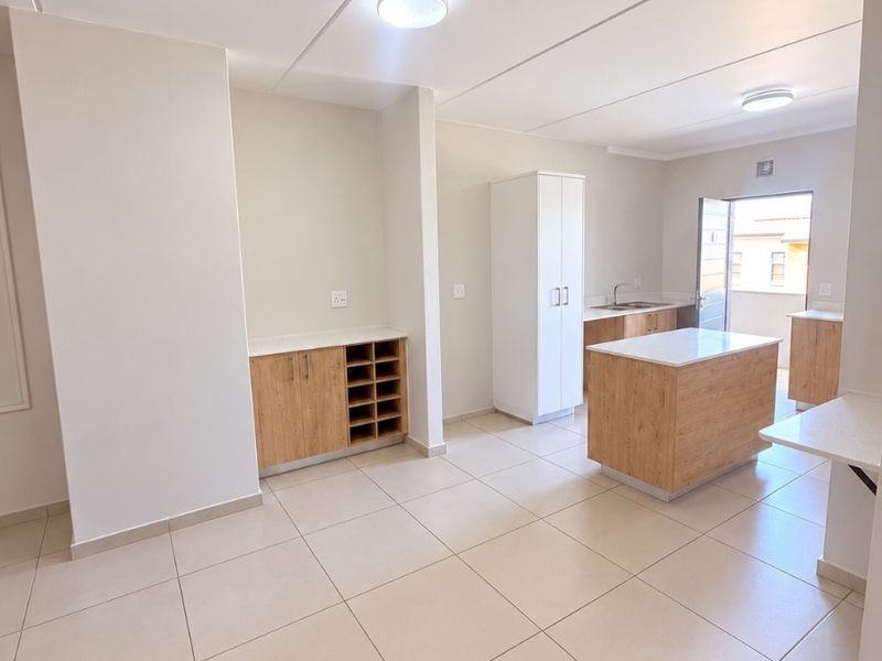 Modern open-plan kitchen and living area featuring light wood cabinetry, a central island, tiled flooring, and direct access to an outdoor balcony.