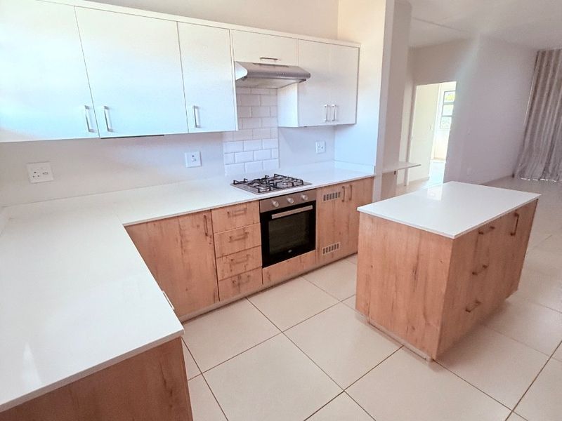 Modern kitchen featuring light wood cabinetry, white stone countertops, a central island, and integrated appliances including a gas hob and oven.