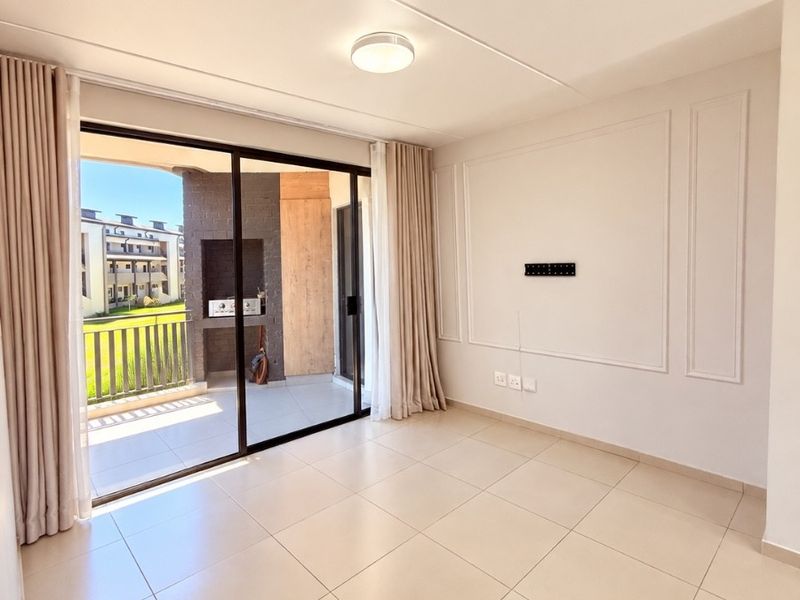 A bright, empty living room featuring large sliding glass doors that open onto a balcony, finished with neutral floor tiles and decorative wall molding.