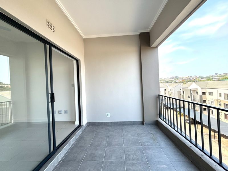 A clean, modern covered balcony featuring grey tiled flooring, a secure metal balustrade, and large sliding glass doors leading into the apartment.
