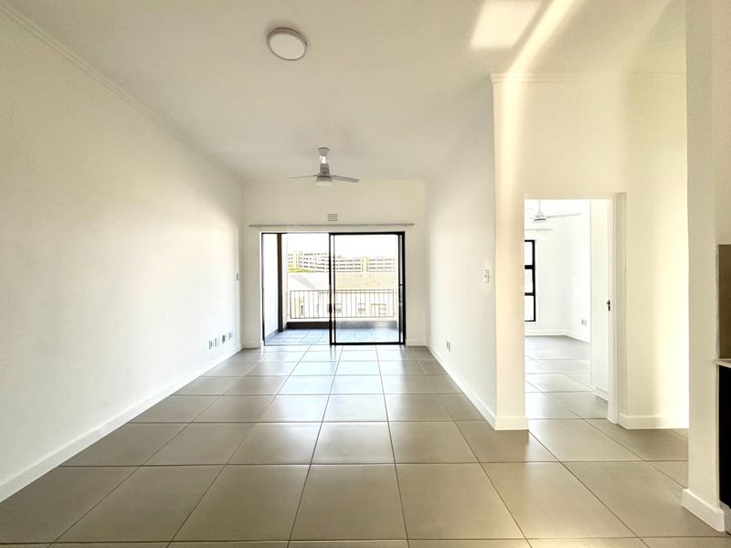 Spacious open-plan living area featuring neutral tiled flooring, a ceiling fan, and direct access to a private balcony through sliding glass doors.