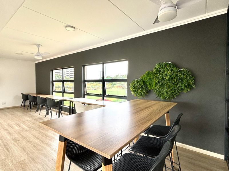 A modern, well-lit office space featuring laminate flooring, ceiling fans, and large windows providing natural light and views.