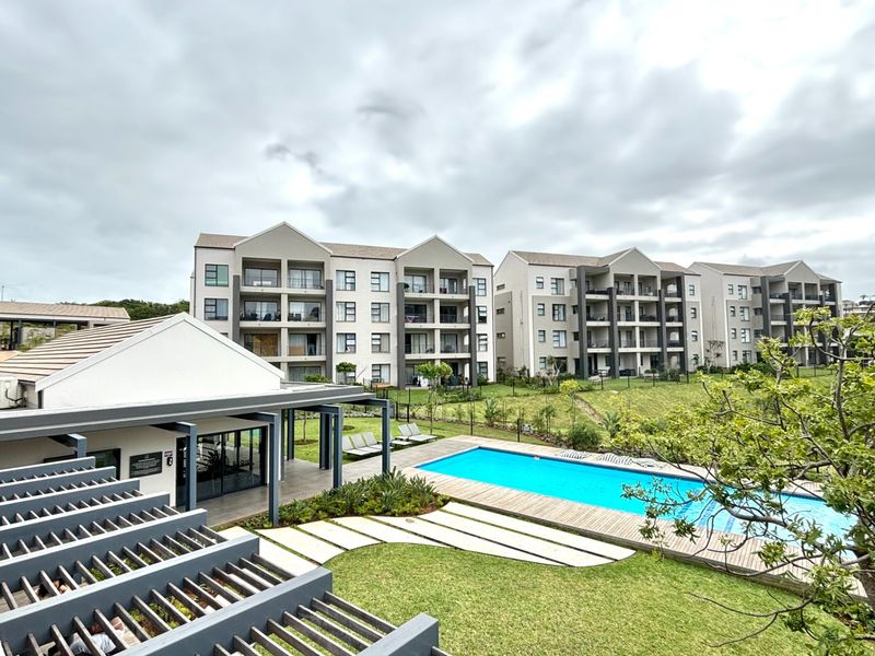 An elevated view of a modern apartment complex featuring a swimming pool, timber decking, landscaped gardens, and a covered pergola area.