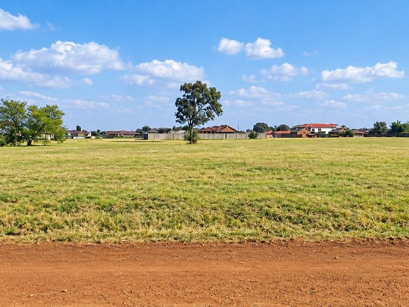 A wide-angle view of a vacant residential plot featuring open grassland, suitable for future development in a suburban neighborhood.