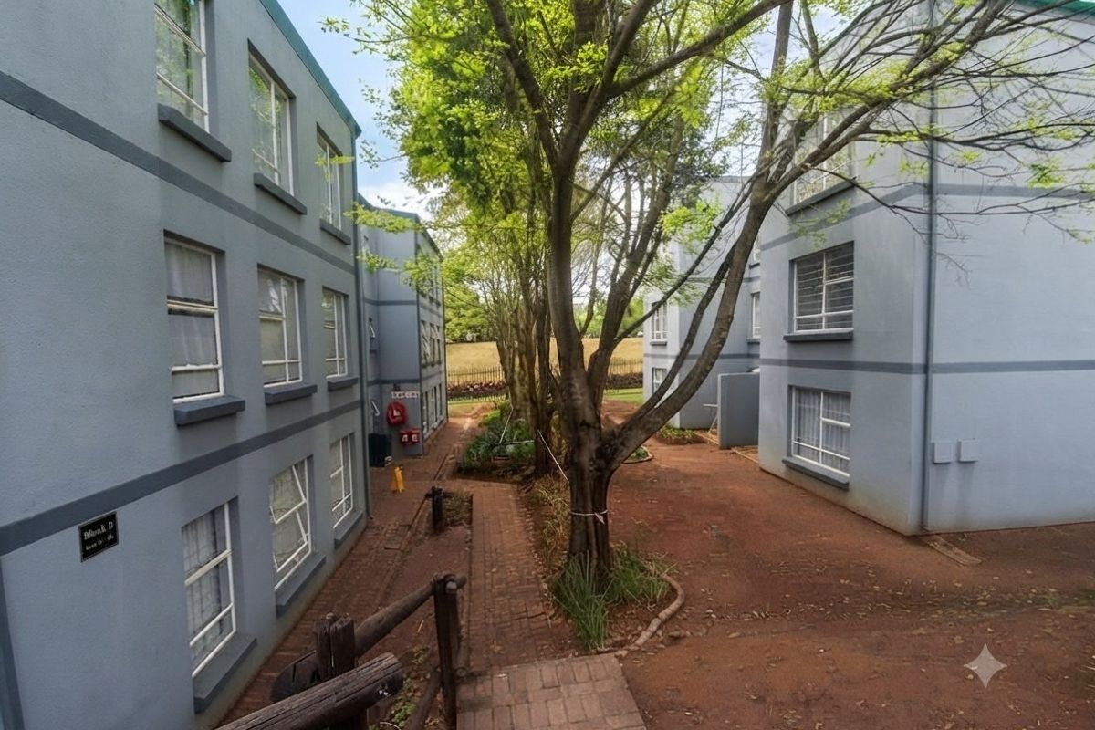 View of the apartment complex exterior showing paved walkways between building blocks and mature trees in the communal garden area.