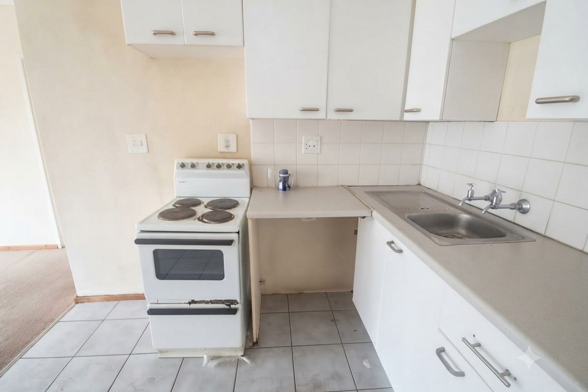 A compact, dated kitchen featuring white cabinetry, a stainless steel sink, and a freestanding electric stove with tiled flooring and backsplash.