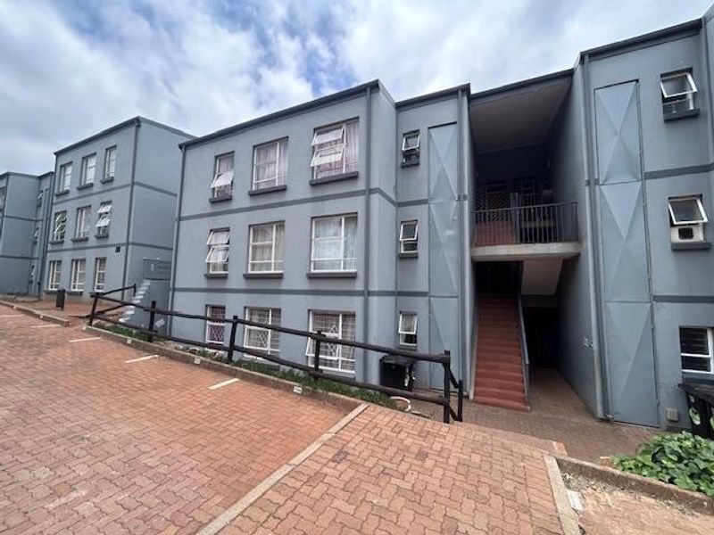 Exterior view of a multi-story apartment complex featuring paved parking, external staircases, and grey painted facade with security-fitted windows.