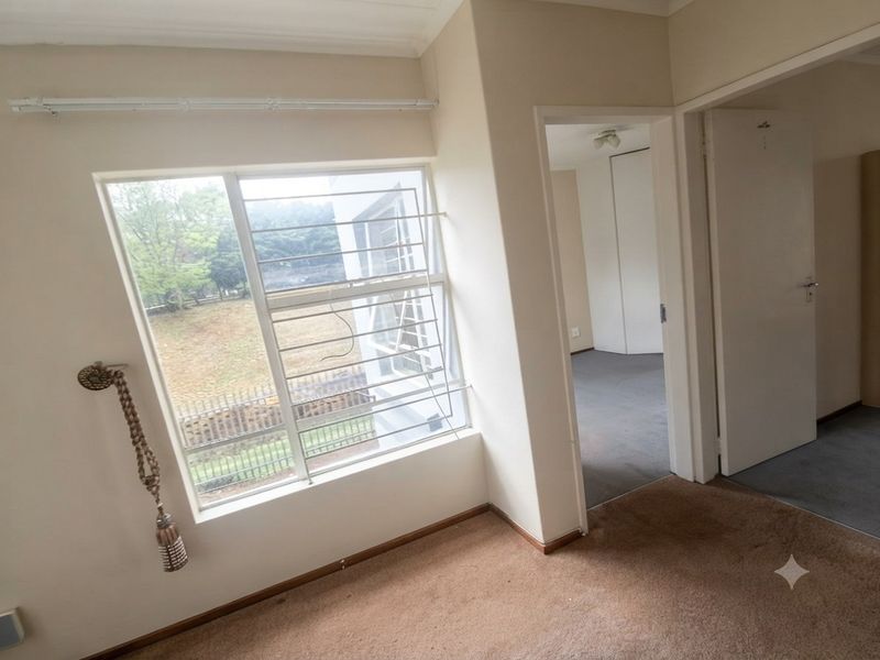 An empty bedroom featuring carpeted flooring, security bars on the window, and a built-in cupboard, offering a blank canvas for renovation.