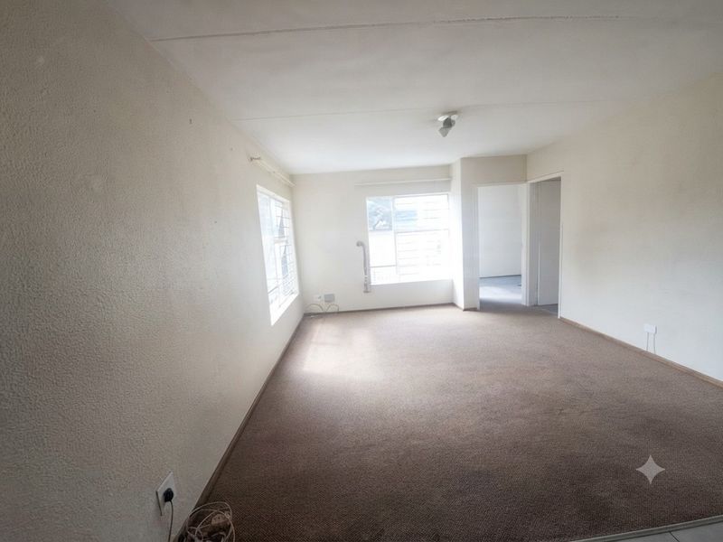 An empty, carpeted living room featuring large windows with security bars, offering a blank canvas for potential interior design and renovation.