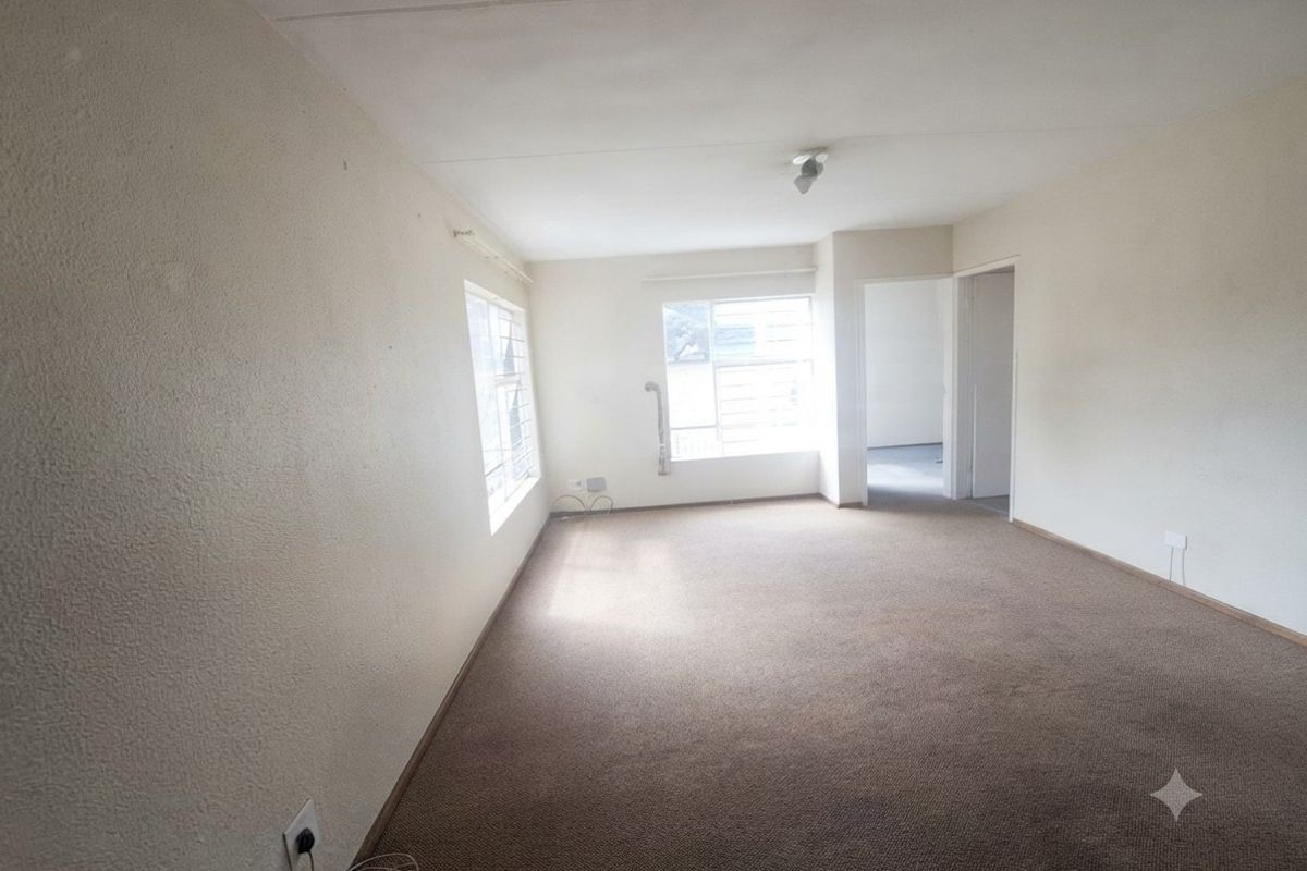 An empty, carpeted living room featuring large windows with security bars, offering a blank canvas for potential interior design and renovation.