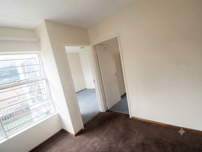 An empty bedroom featuring carpeted flooring, security bars on the window, and access to adjacent rooms through internal doorways.