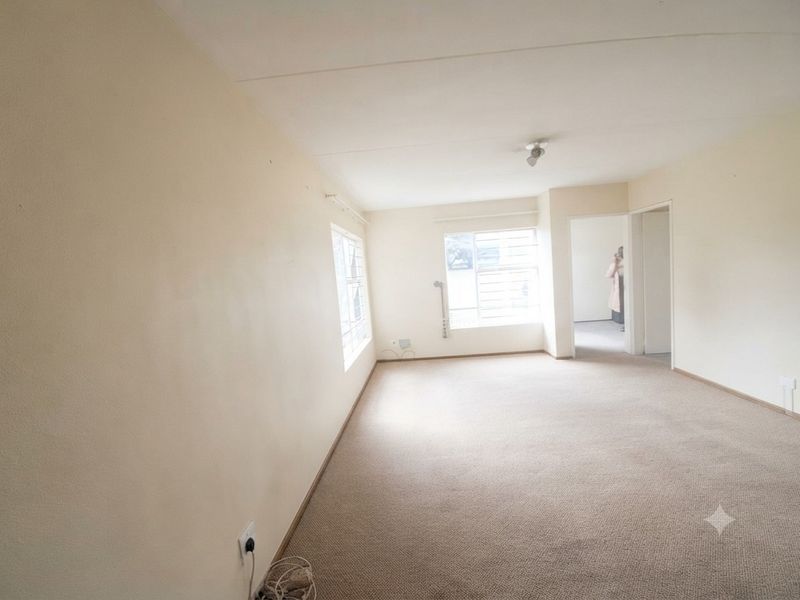 A spacious, empty living room featuring neutral walls, carpet flooring, and security bars on the windows, offering a blank canvas for potential updates.