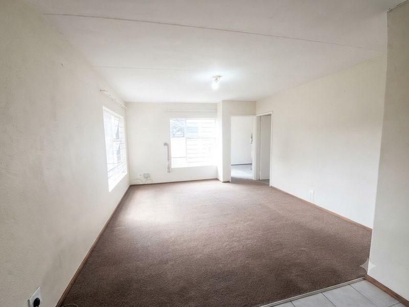 An empty living room featuring brown carpet flooring, neutral walls, and security bars on the windows, offering a blank canvas for potential updates.