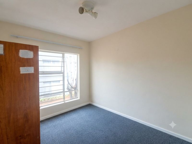 An empty bedroom featuring carpet flooring, a louvered window, and a ceiling-mounted light fixture, ready for personalization.