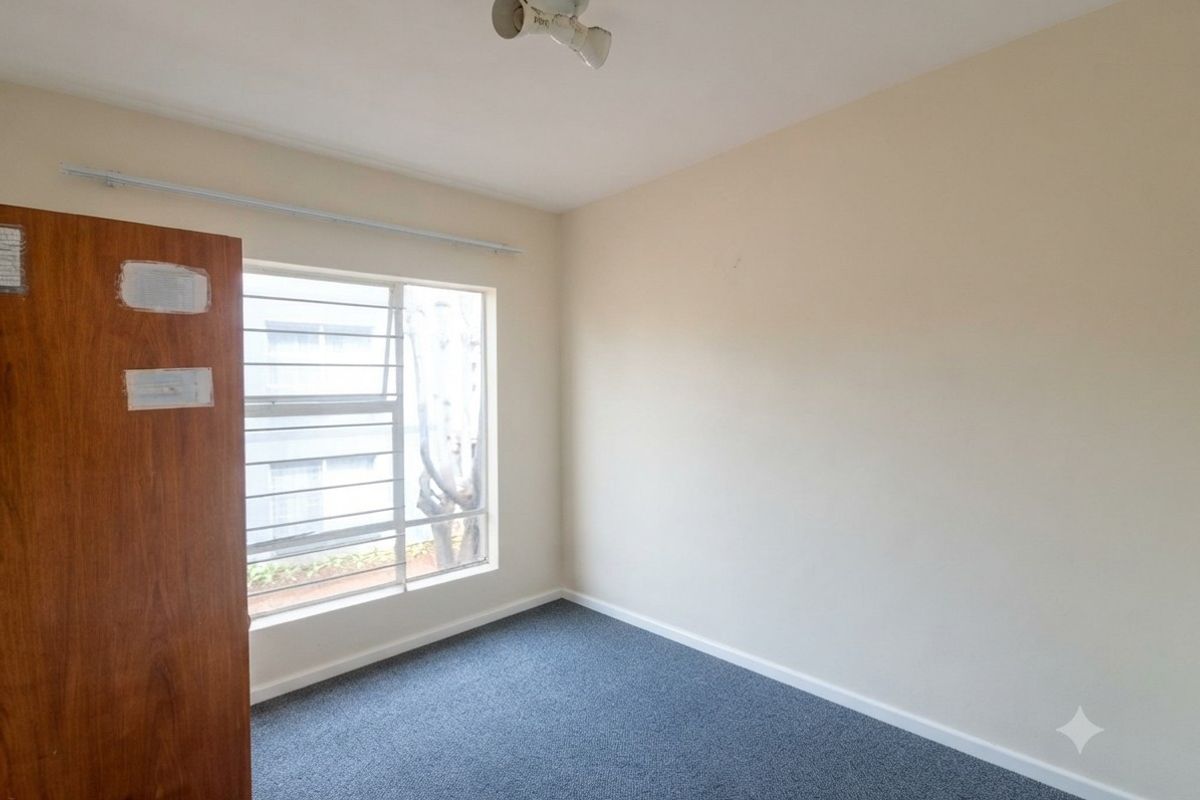 An empty bedroom featuring carpet flooring, a louvered window, and a ceiling-mounted light fixture, ready for personalization.