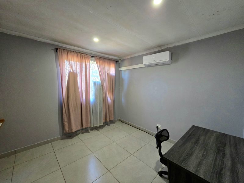 A functional bedroom featuring tiled flooring, a wall-mounted air conditioning unit, and recessed lighting, providing a neutral base for personalization.