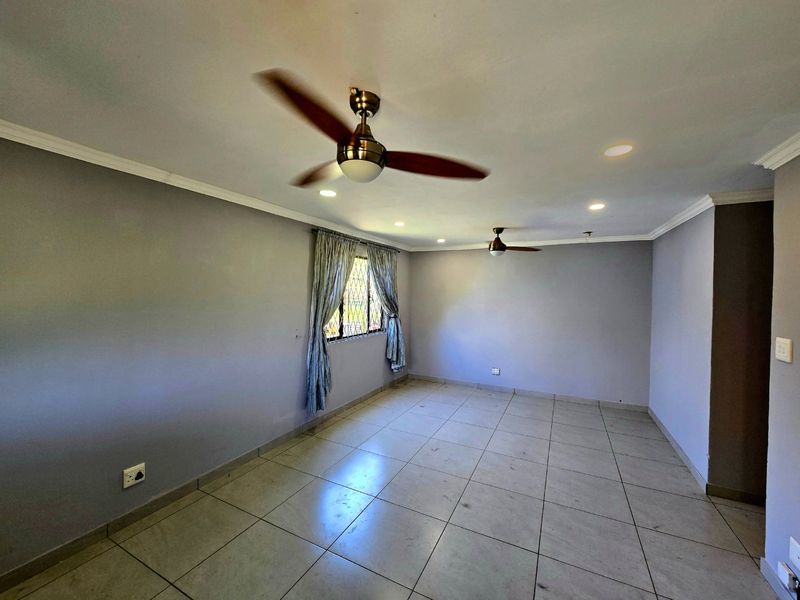 Spacious, empty living area featuring neutral grey walls, tiled flooring, recessed lighting, and dual ceiling fans.