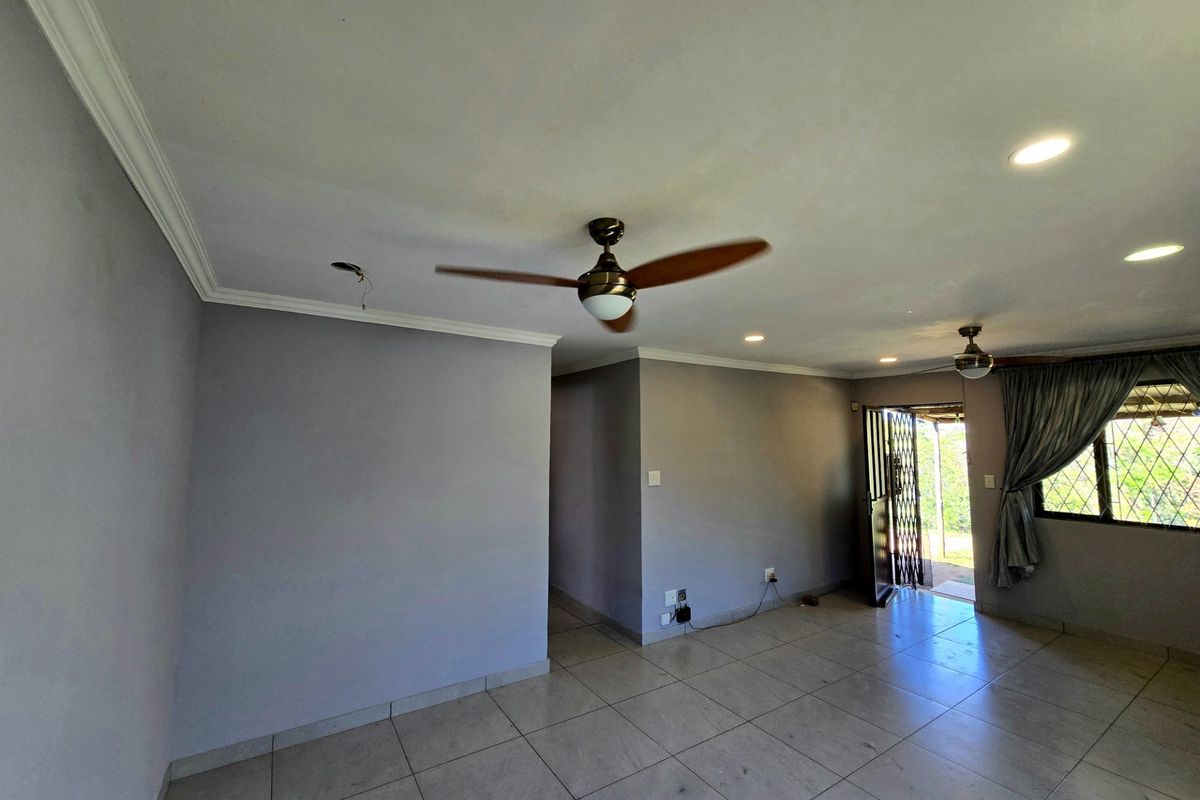 An empty living room featuring tiled flooring, recessed lighting, and ceiling fans, with direct access to an outdoor area through a security gate.