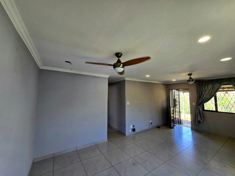 An empty living room featuring tiled flooring, recessed lighting, and ceiling fans, with direct access to an outdoor area through a security gate.