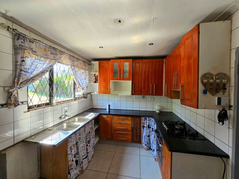 A functional kitchen featuring wooden cabinetry, granite countertops, a double basin sink, and a built-in gas hob with oven, requiring some cosmetic updates.