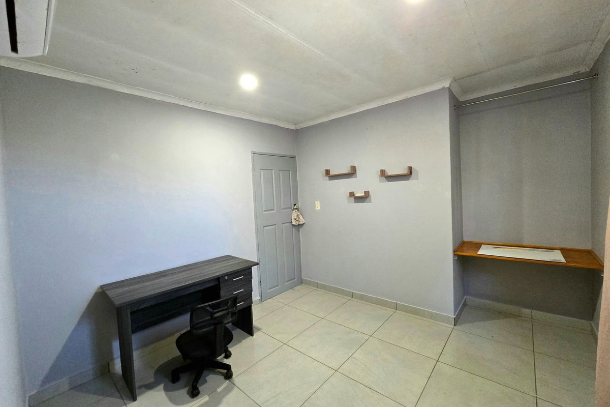 A functional bedroom featuring tiled flooring, a built-in desk area, wall-mounted shelving, and an air conditioning unit.