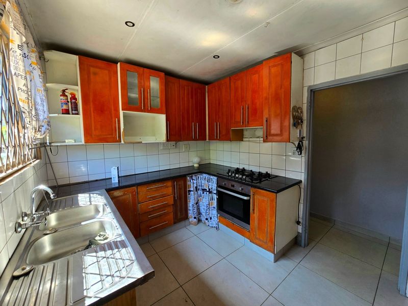 Functional kitchen featuring wooden cabinetry, a gas hob, built-in oven, and double bowl sink with tiled backsplash and flooring.