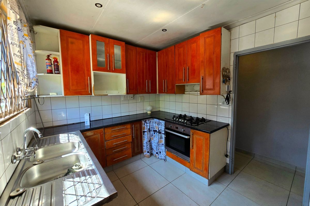 Functional kitchen featuring wooden cabinetry, a gas hob, built-in oven, and double bowl sink with tiled backsplash and flooring.
