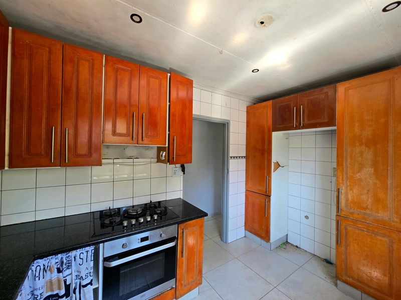 A dated kitchen featuring wooden cabinetry, granite countertops, a gas hob, and an integrated oven, requiring cosmetic updates to modernize the space.