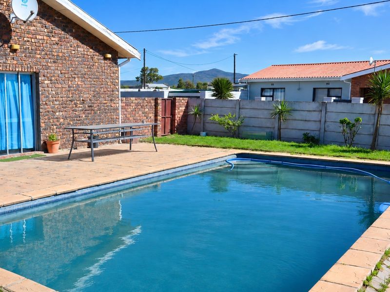Outdoor pool area featuring a paved patio, brick exterior wall, and a precast concrete boundary wall in a residential backyard setting.