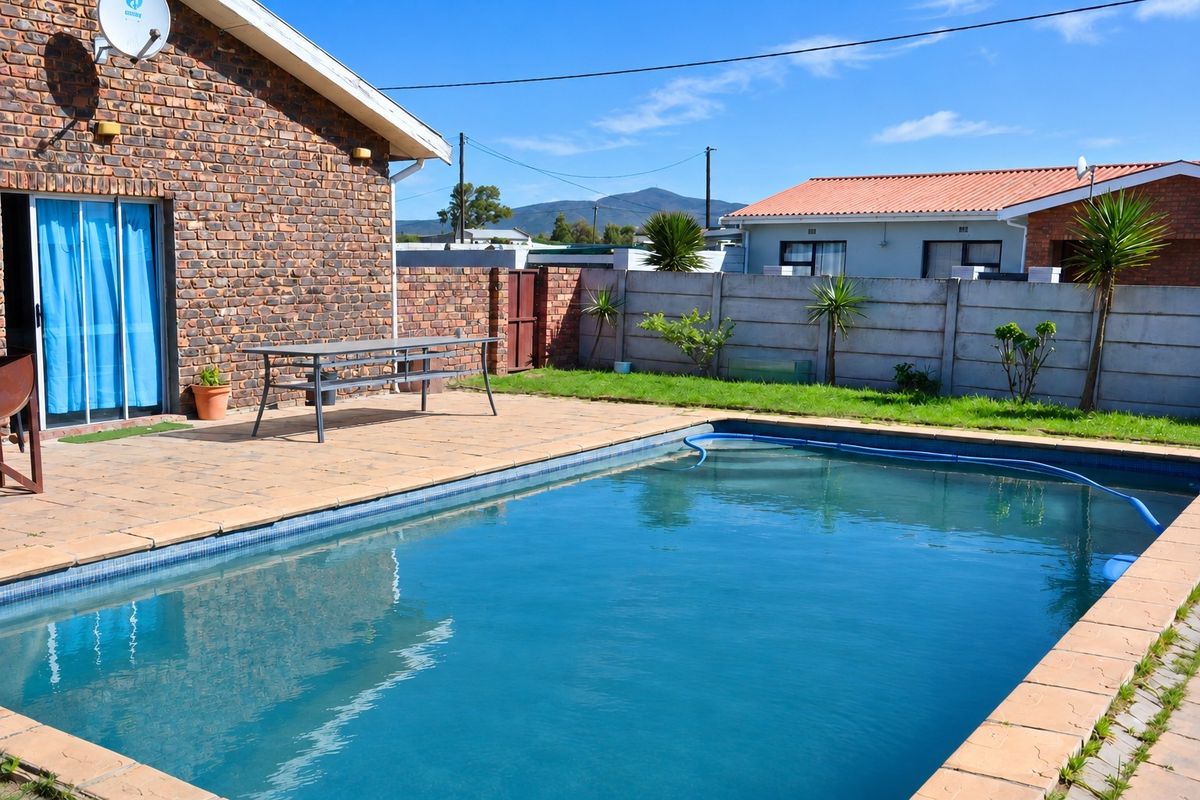 Outdoor pool area featuring a paved patio, brick exterior wall, and a precast concrete boundary wall in a residential backyard setting.