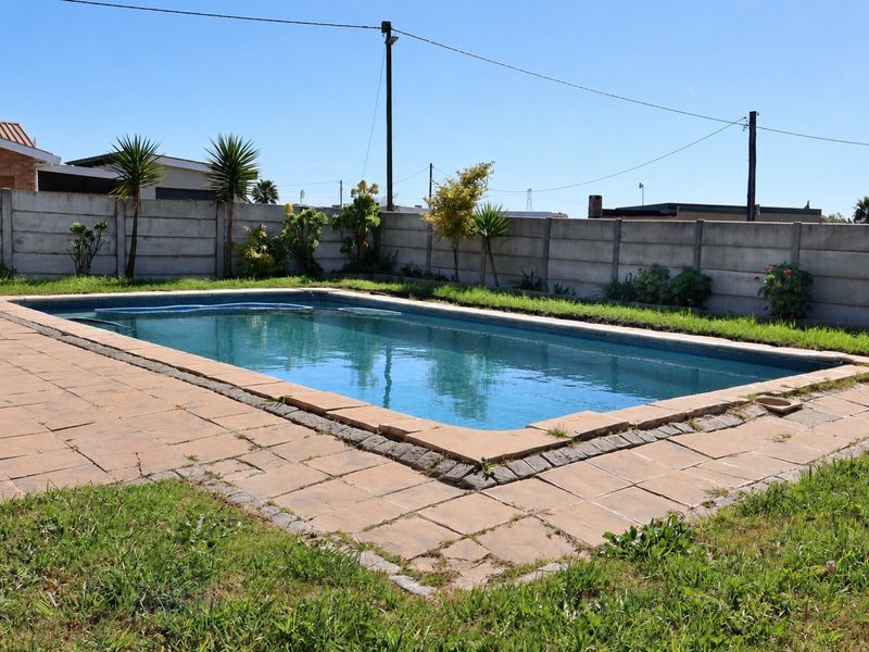 Outdoor swimming pool area featuring a paved surround and a precast concrete boundary wall.