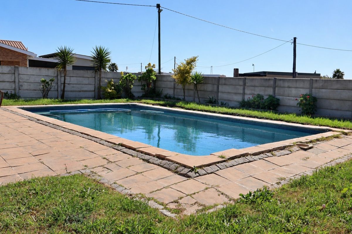 Outdoor swimming pool area featuring a paved surround and a precast concrete boundary wall.