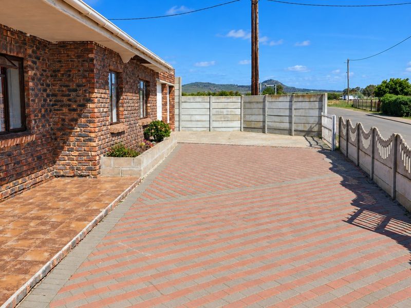 A neat front exterior featuring a face brick facade, a tiled patio, and a paved driveway enclosed by precast concrete boundary walls.