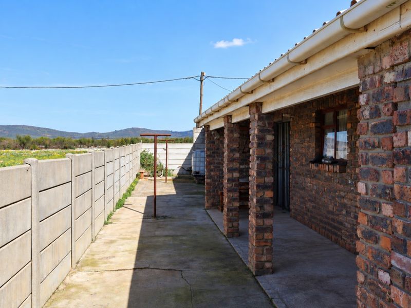 A covered outdoor patio area featuring brick pillars and concrete flooring, adjacent to a precast boundary wall with views of the surrounding landscape.
