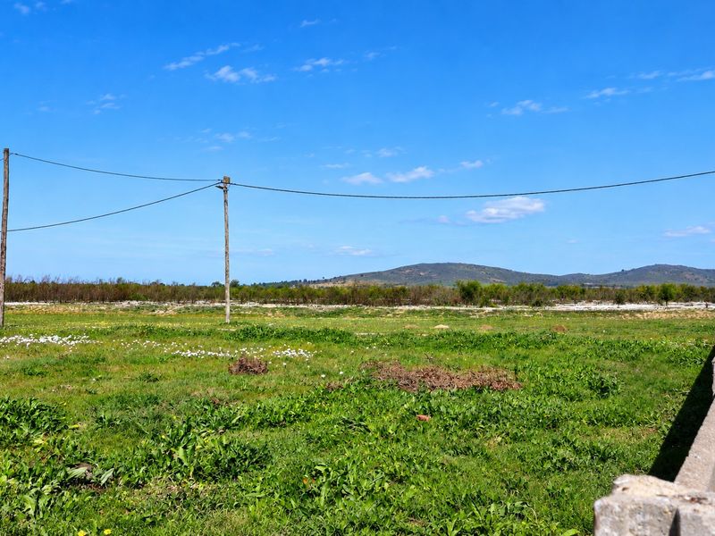 A wide-angle view of an open grassy field with distant hills, featuring utility poles and a concrete boundary wall in the foreground.