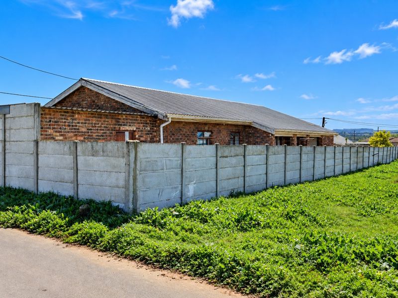 Rear view of a facebrick house enclosed by a precast concrete boundary wall, featuring a corrugated metal roof and surrounding grass area.