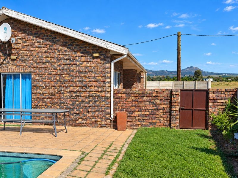 Rear exterior view featuring a brick facade, paved patio area, swimming pool, and a private garden with a metal access gate.