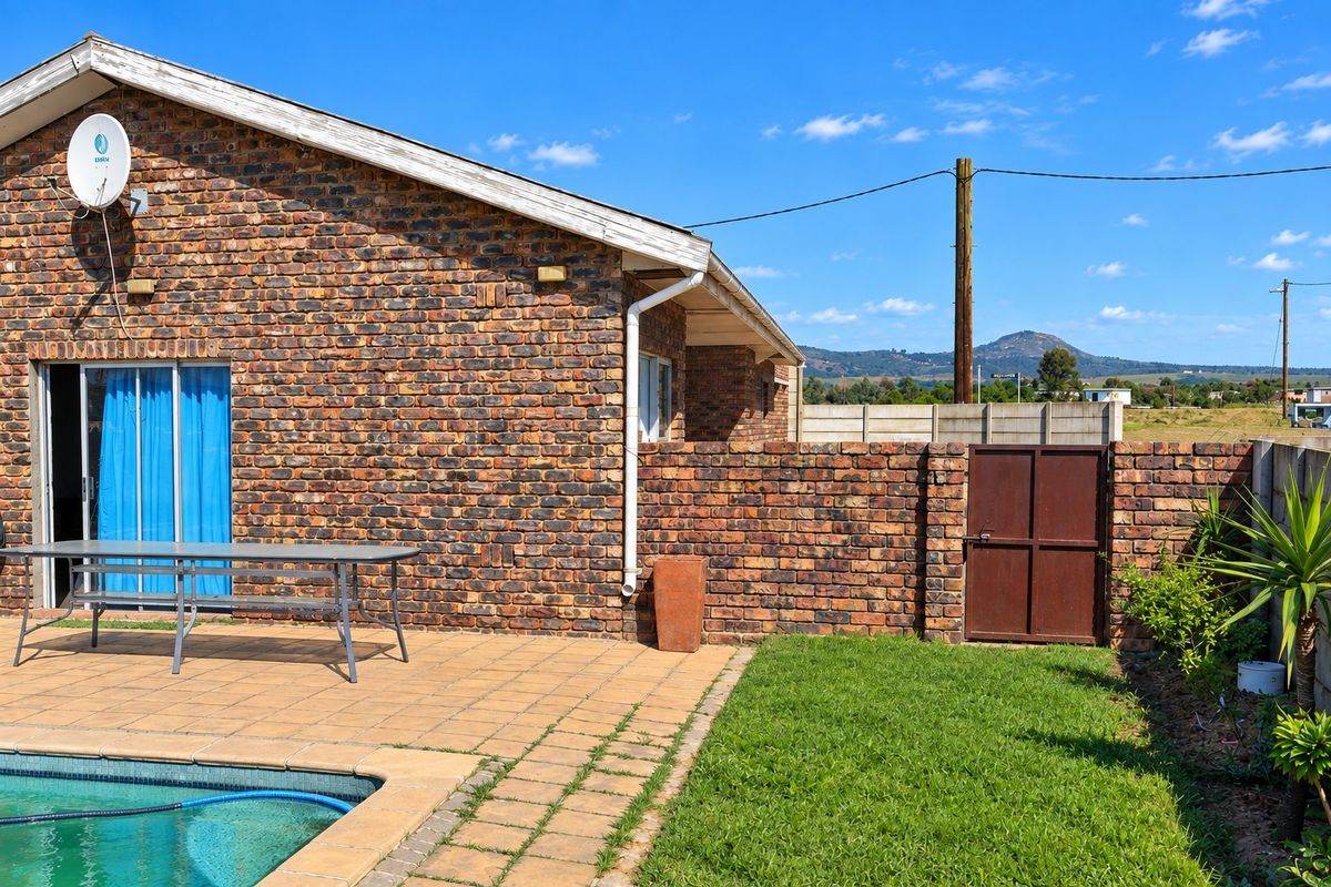 Rear exterior view featuring a brick facade, paved patio area, swimming pool, and a private garden with a metal access gate.