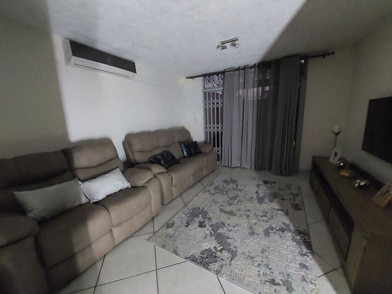 A comfortable living room featuring tiled flooring, a wall-mounted air conditioning unit, and a security gate leading to the exterior.