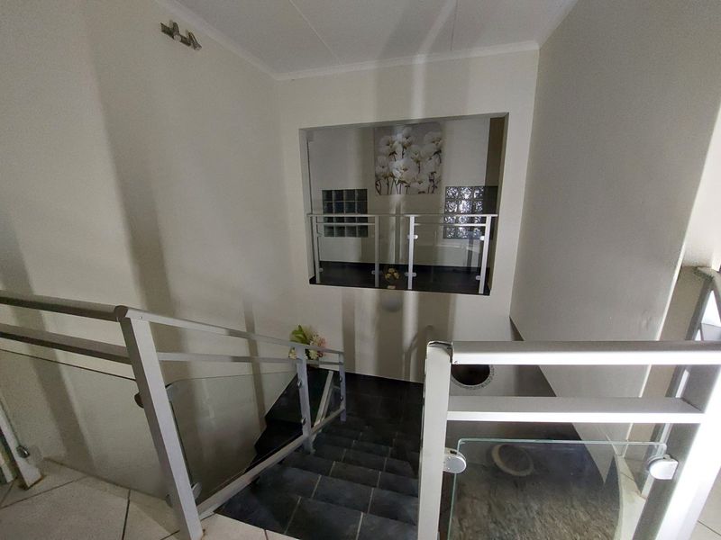 A bright staircase area featuring modern glass balustrades, metal handrails, and decorative glass block accents.