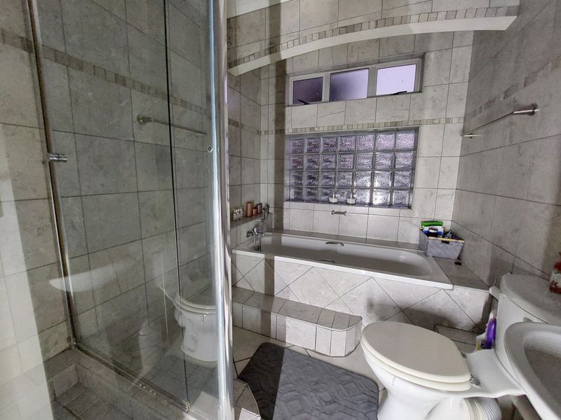 A functional bathroom featuring a built-in bathtub, separate glass shower enclosure, toilet, and pedestal sink with neutral tiled finishes throughout.
