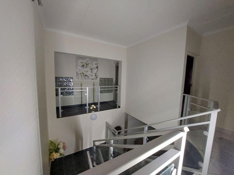 A bright hallway featuring a modern staircase with glass balustrades and a decorative glass block feature wall.