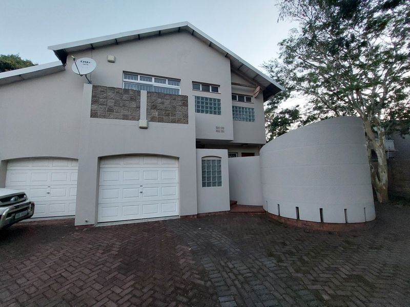 Front elevation of a townhouse featuring a double garage, paved driveway, and distinctive curved architectural wall detail.