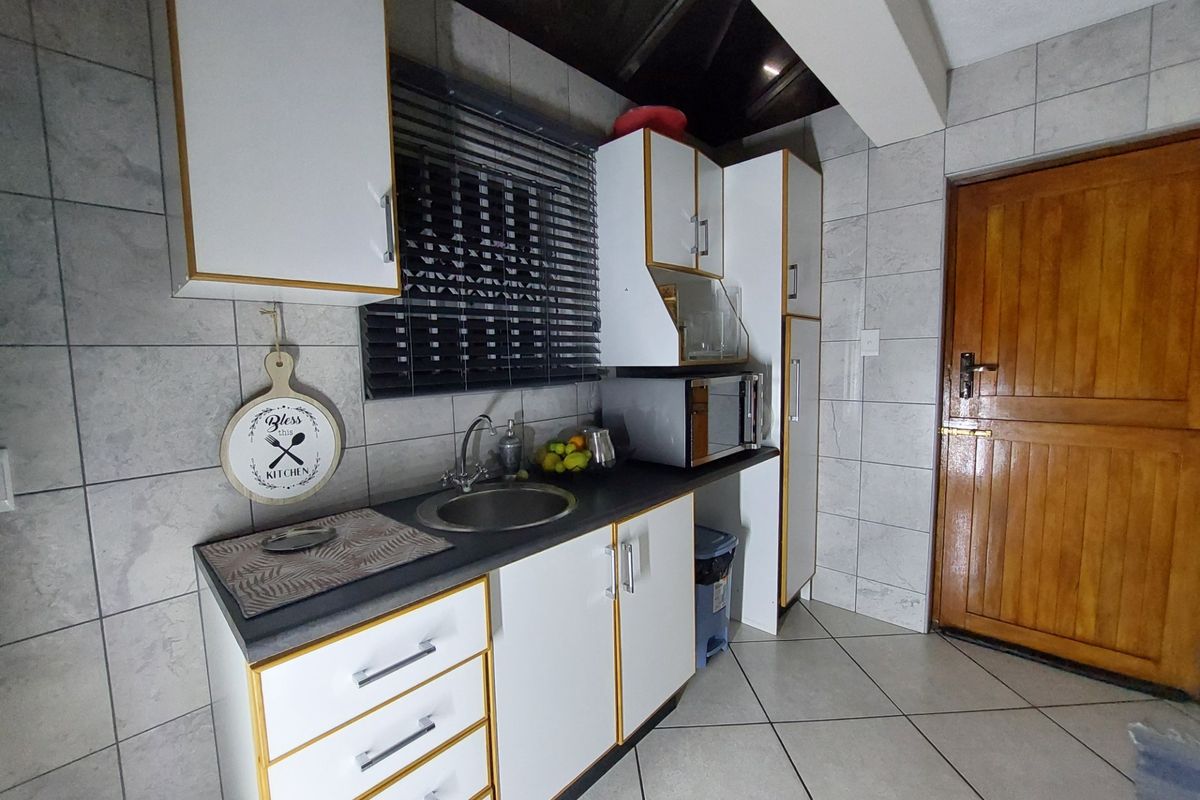 Compact kitchen featuring white cabinetry with contrasting trim, tiled backsplash, stainless steel sink, and tiled flooring, providing a functional prep area.